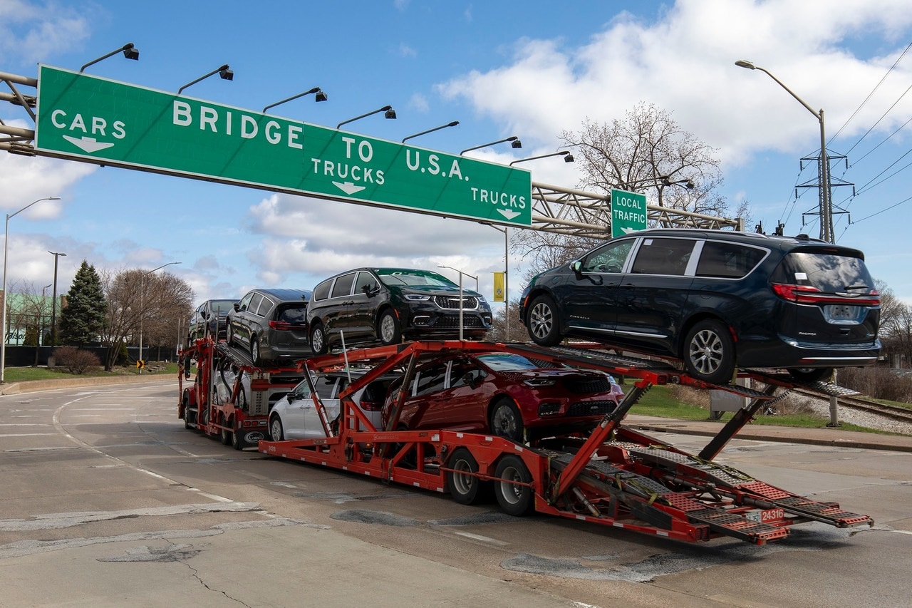 cars being transported on semi trailer; sign shows "Bridge to U.S.A."